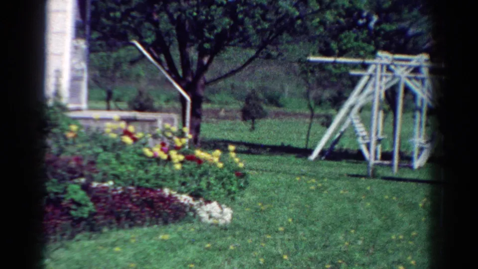 1954 Toledo frame with a flower bed in the foreground, a tree near the house, and a wooden swingset across the lawn.