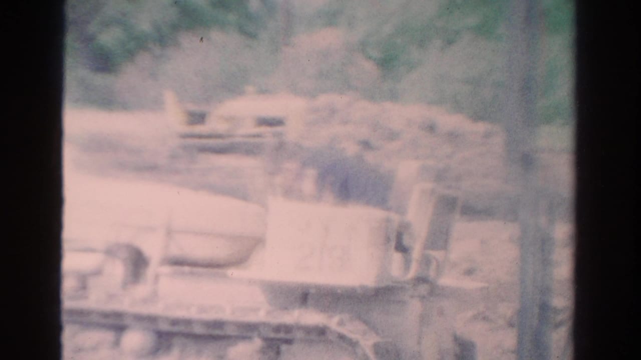 Soft 8mm frame from the Toledo clip with pale, overexposed construction equipment partly visible in a green outdoor setting.
