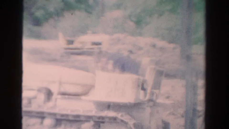 Soft 8mm frame from the Toledo clip with pale, overexposed construction equipment partly visible in a green outdoor setting.