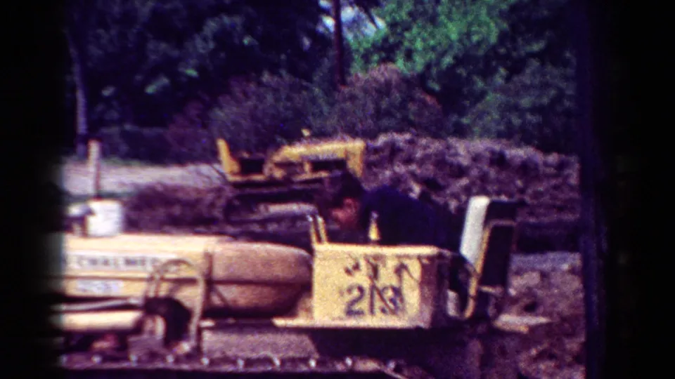 1954 Toledo 8mm frame showing the yellow bulldozer and seated operator against trees and a low pile of earth or brush.