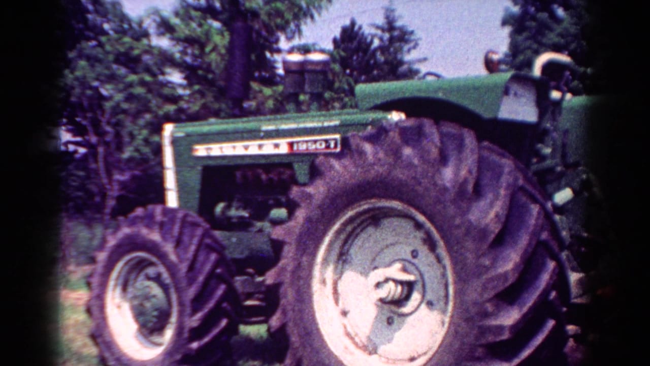 1954 Toledo-area home-movie frame showing a green Oliver tractor in a field, with large treaded tires and trees behind it.