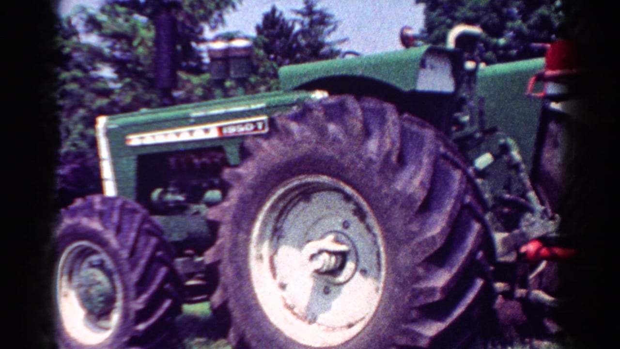 Close view of green tractor side, large rear wheel, and partial red implement at the back.