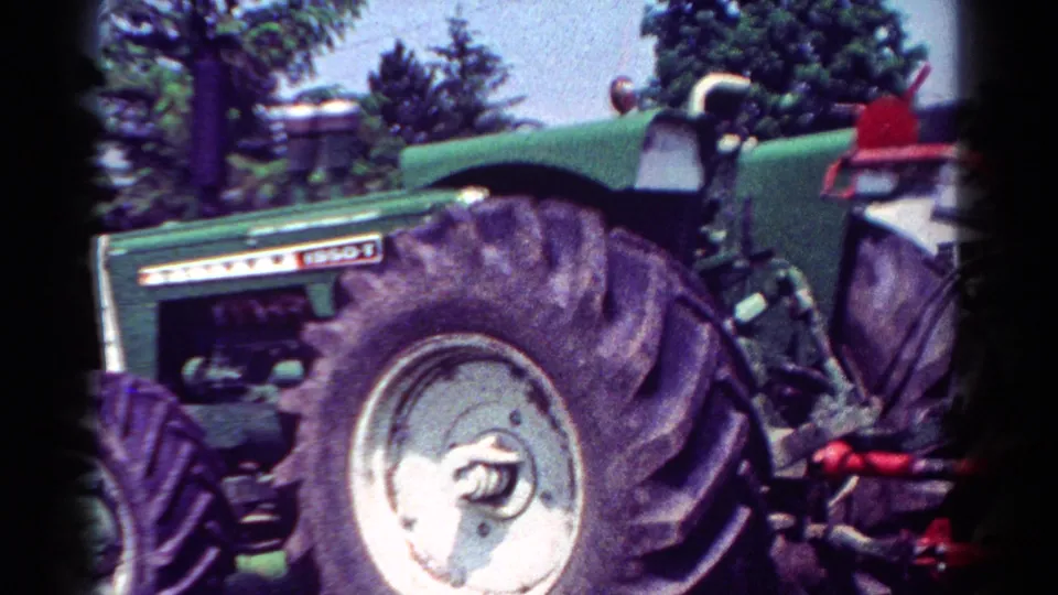Close 8mm frame of a green Oliver tractor in a field, showing the large rear wheel and red implement at the back.