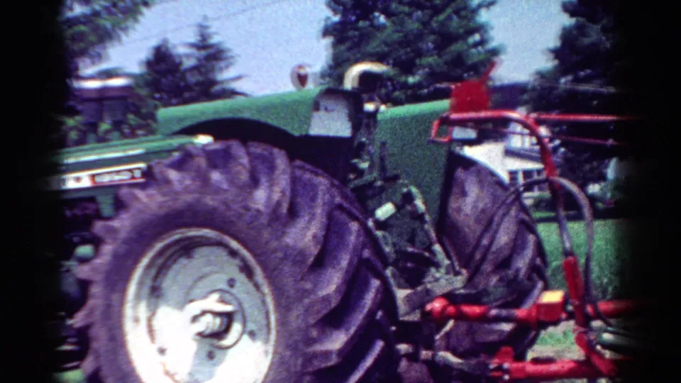 Final 1954 home-movie frame showing the rear side of the green Oliver tractor and red implement in a leafy field setting.