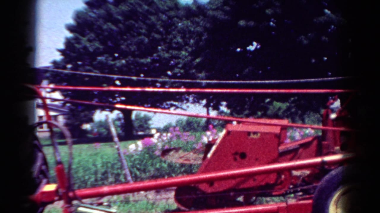Red tractor machinery crosses the foreground with trees and garden behind.