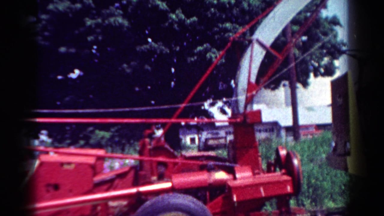 Red chipper and chute in front of trees, with a building partly visible behind.