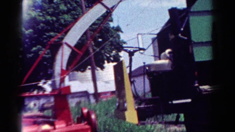 1954 Toledo frame showing the red chipper beside a green dump truck, with grass, trees, wires, and a house in the background.