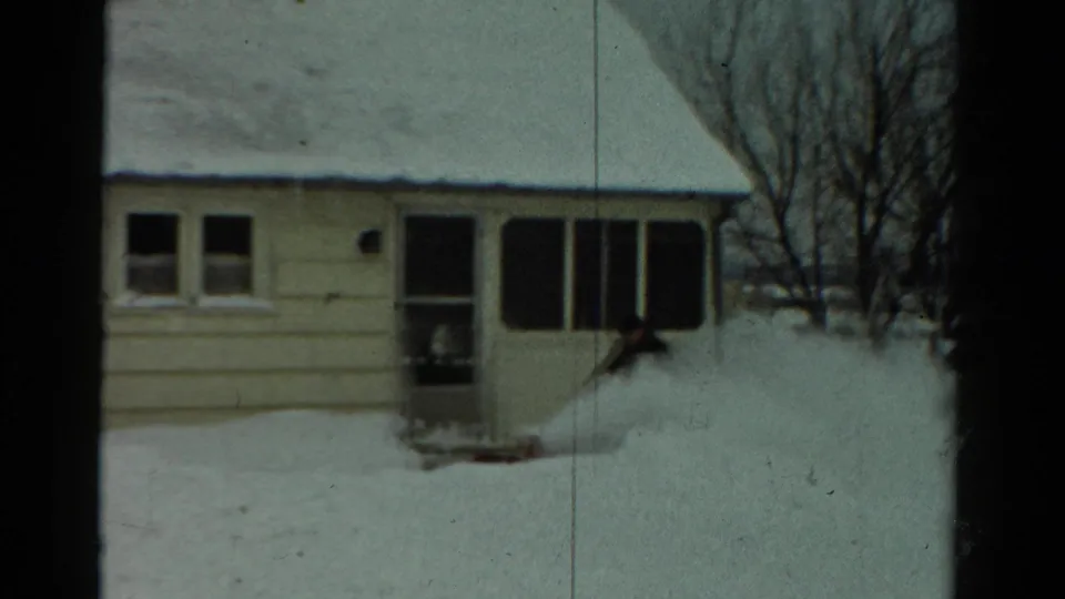 A modest Toledo house sits behind deep snow as a person clears a path near the front entrance in winter.