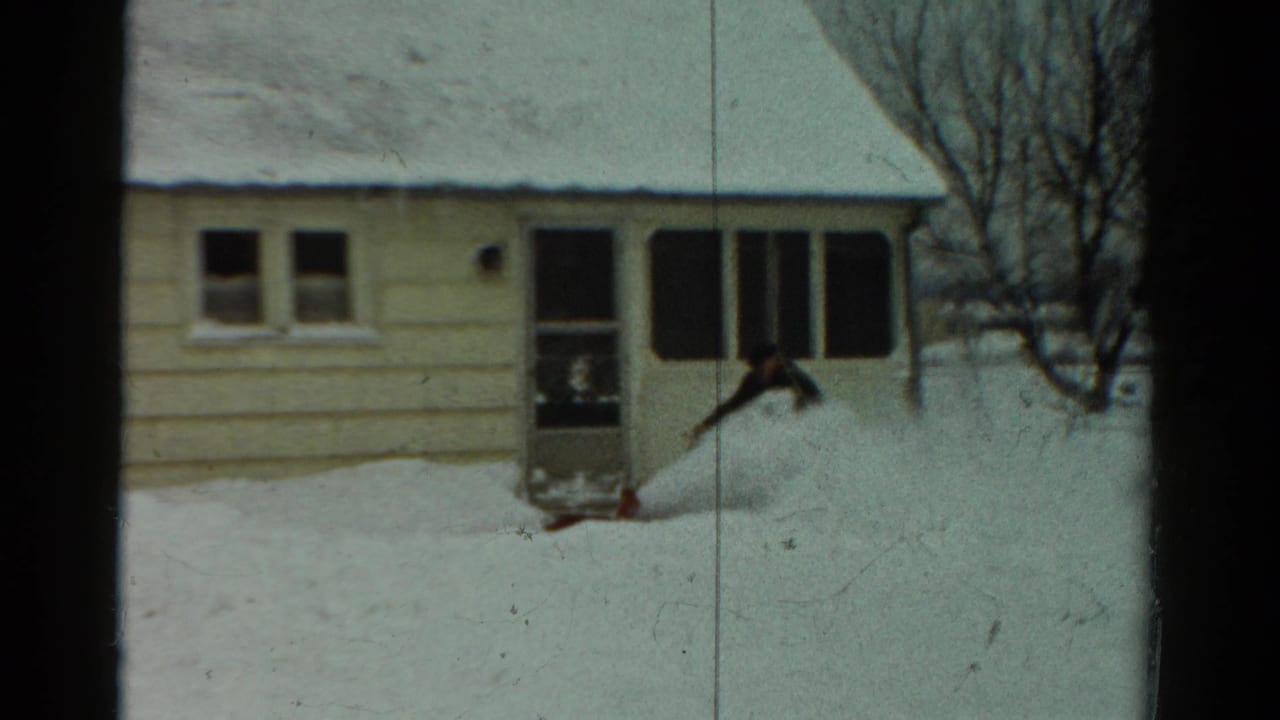 In 1954 Toledo, Ohio footage, a man in dark winter clothing clears deep snow near a light-colored house with a porch.