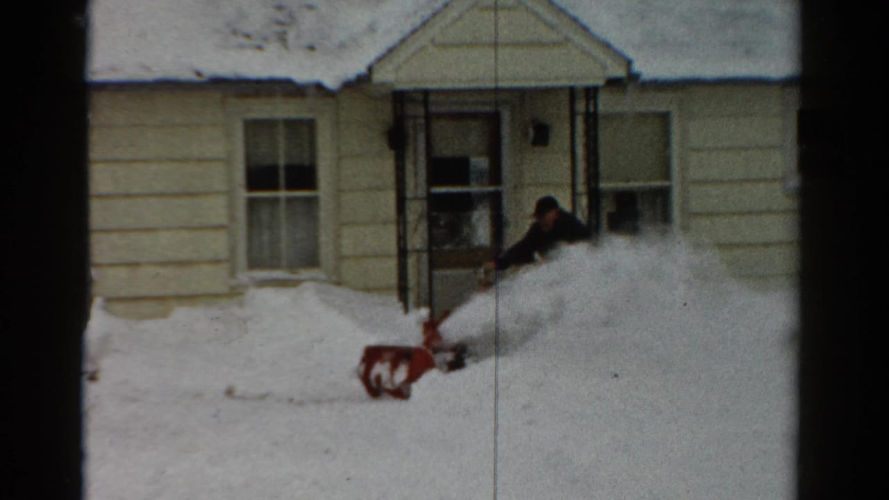 Snow blower throws snow beside the front door as the man works outside the house.