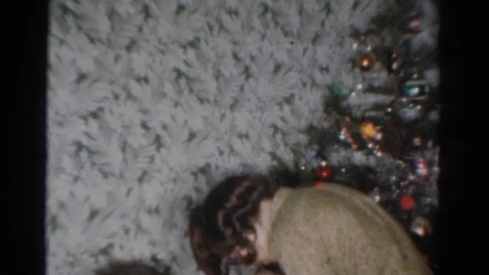 The final frame holds on the younger woman leaning beside the Christmas tree, with the older woman partly visible below.