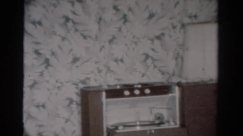 A mid-century radio or record-player console sits against floral wallpaper in the Toledo home interior, with no face visible in this frame.
