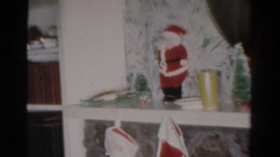 1954 Toledo living-room frame with Santa figurine, small tree decoration, books, and floral wallpaper.
