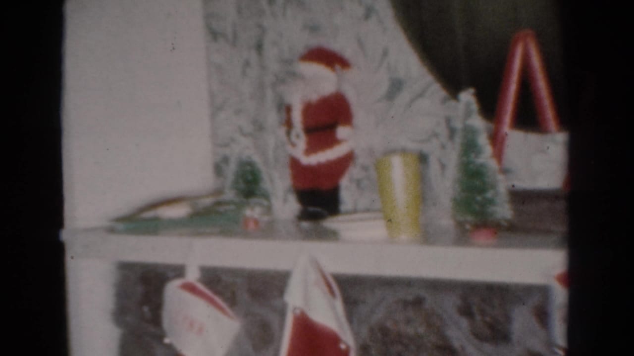 1954 Toledo 8mm frame showing a Christmas mantel display with a Santa figurine, miniature trees, red decorations, and stockings.