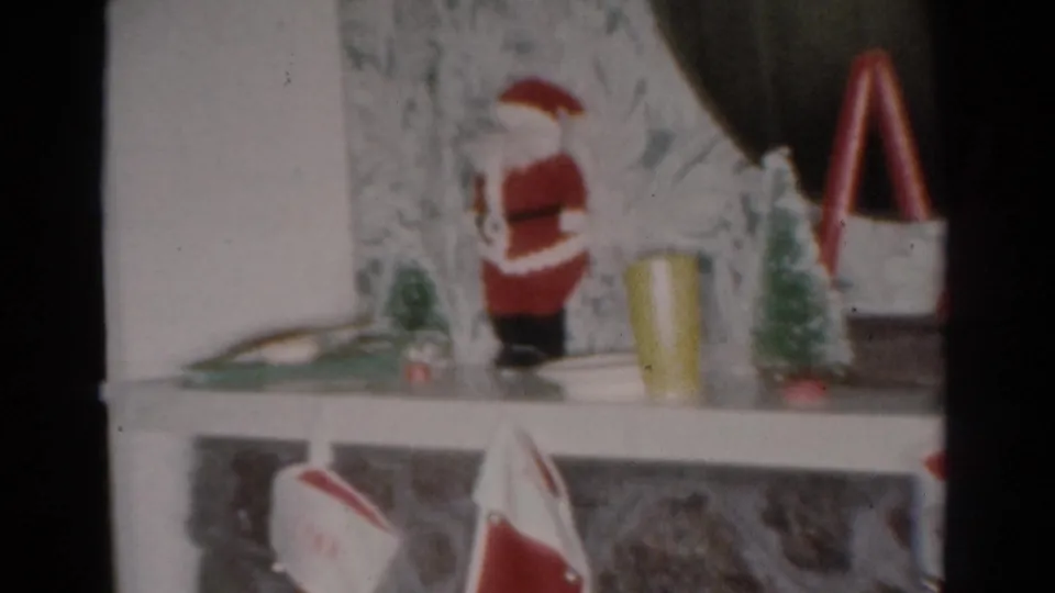 1954 Toledo 8mm frame showing a Christmas mantel display with a Santa figurine, miniature trees, red decorations, and stockings.