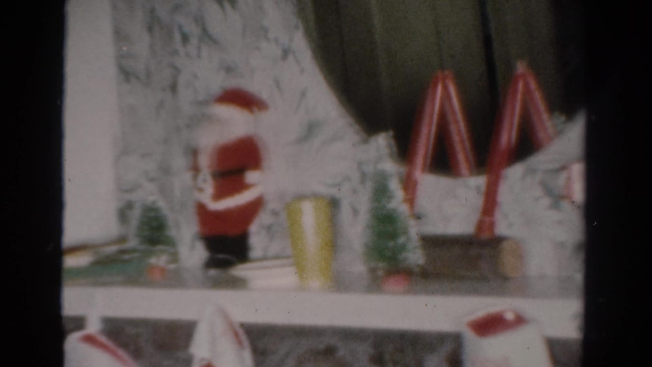 Soft-focus mantel display with Santa figure, small tree, yellow cup, and red arched decorations.