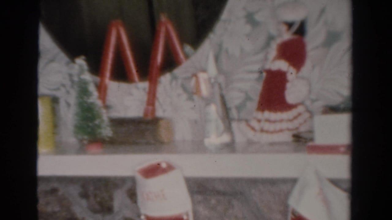 1954 Toledo home-movie frame showing a small Christmas display on a shelf with red candles, miniature tree, and holiday figurine.