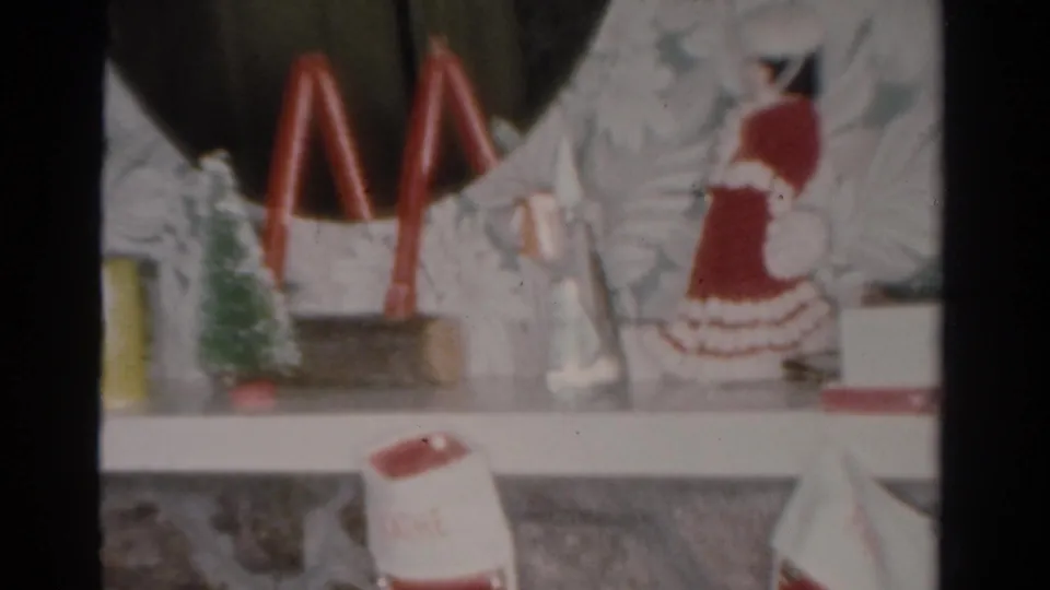 1954 Toledo home-movie frame showing a small Christmas display on a shelf with red candles, miniature tree, and holiday figurine.