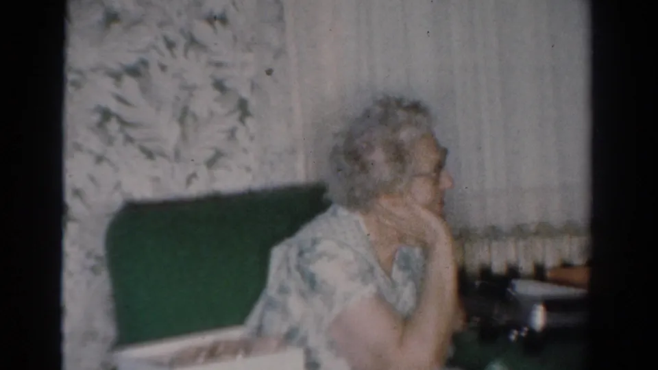 1954 Toledo home-movie frame showing an older woman on a green couch, turned toward the room beside Christmas decor.