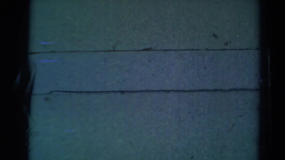Soft 8mm frame with a pale surface, horizontal plank-like lines, and dark edge shapes; the supplied metadata notes a partial face in the clip.