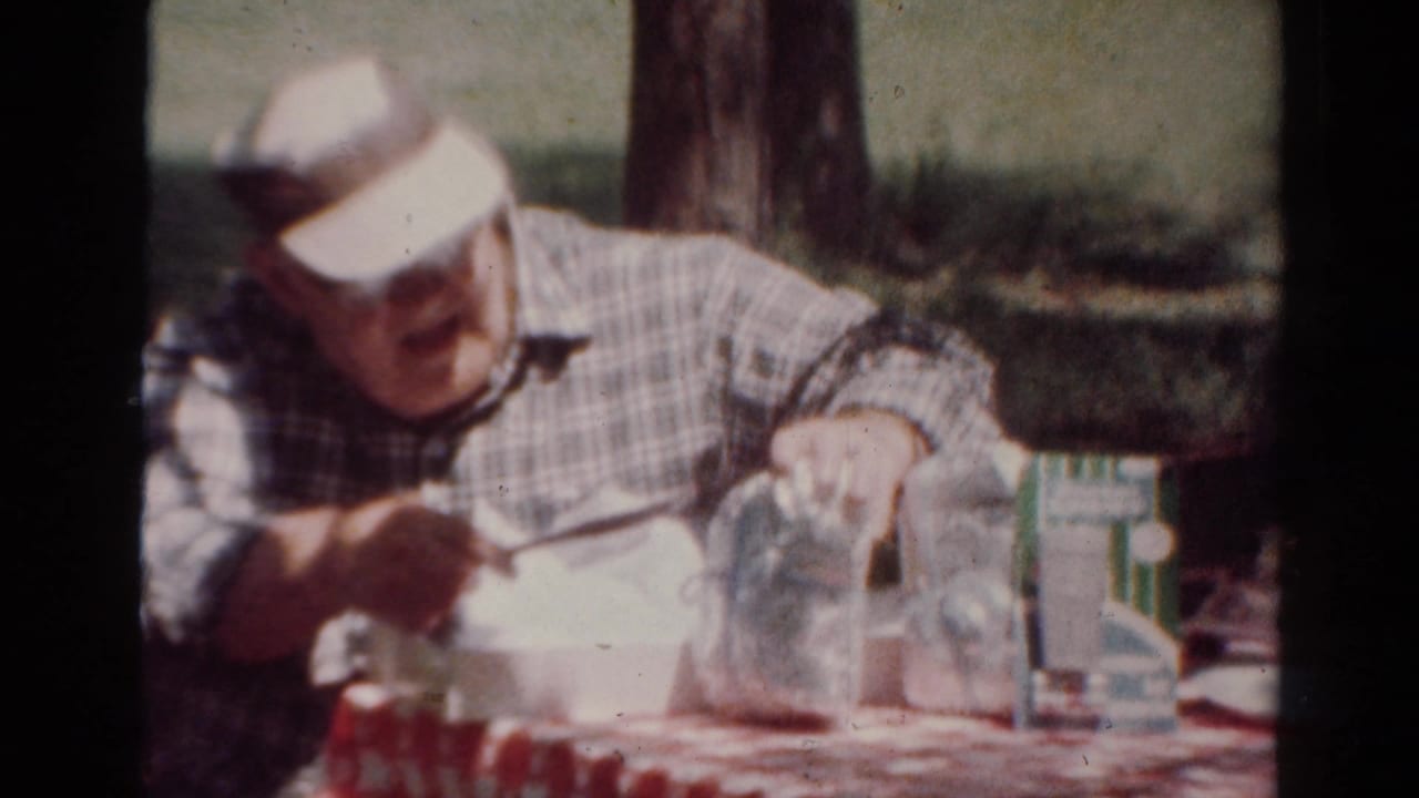 In the Toledo picnic scene, the man leans forward over a white food container with glass jars on the table.