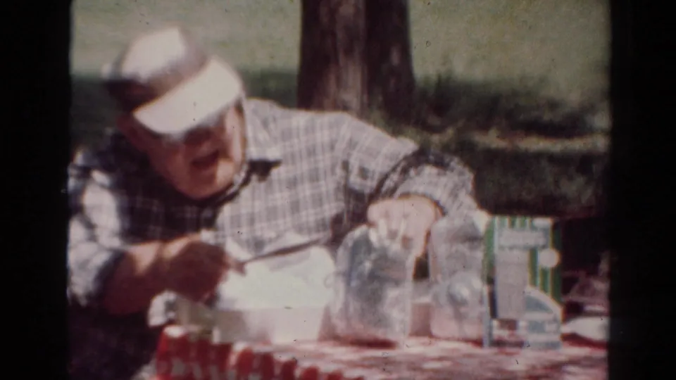 In the Toledo picnic scene, the man leans forward over a white food container with glass jars on the table.