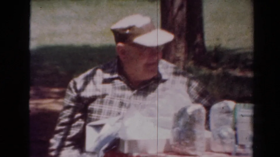 The man remains seated beside picnic items in a shaded Toledo park scene, with trees and grass behind him.