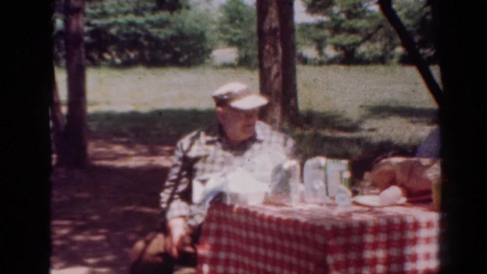 A wider 1954 Toledo park view shows the man beside a checkered picnic table with food, bottles, cups, and wooded shade.