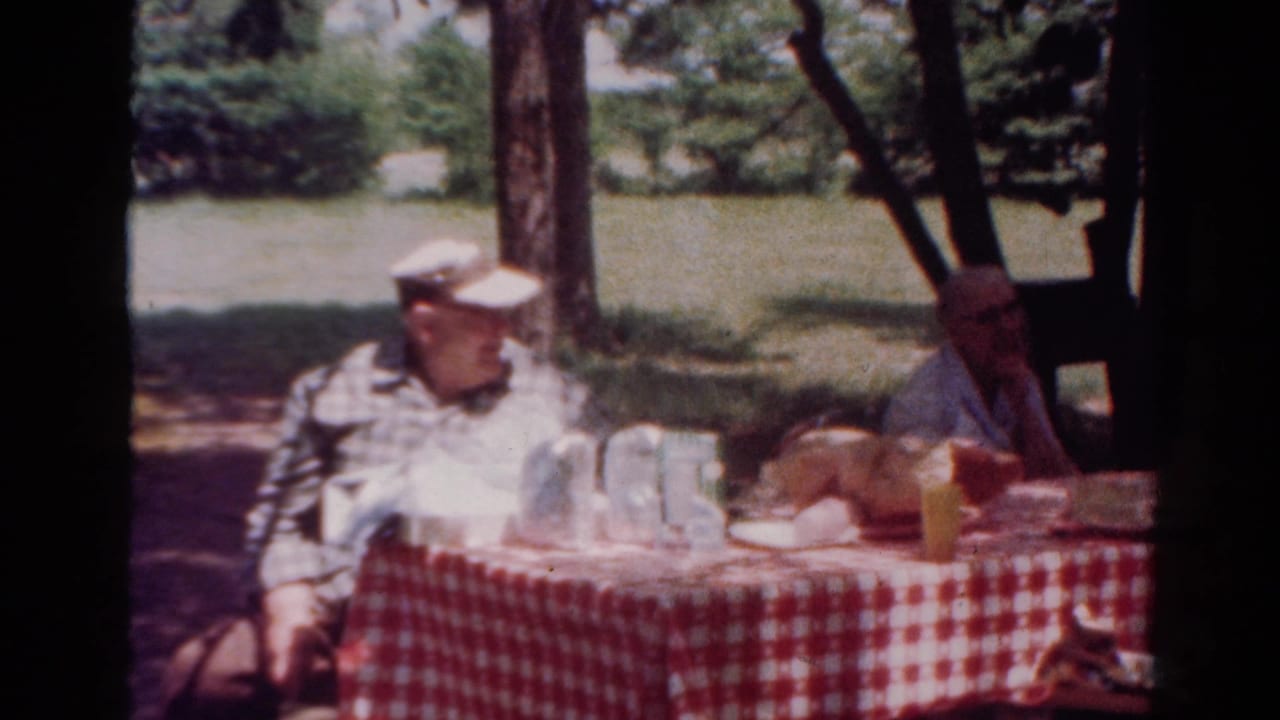 1954 Toledo outdoor picnic scene with an older man in a cap and another adult seated across a checked table.