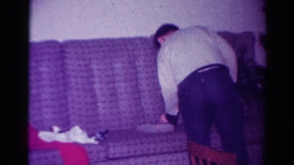 1954 Toledo home-movie frame showing a person in a light sweater leaning over a couch during Christmas gift activity.