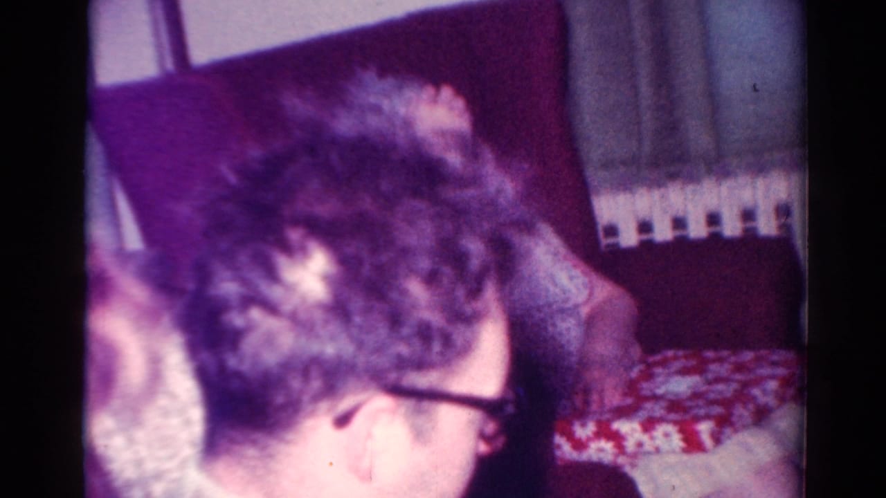 Man with glasses leans over near a patterned gift box in a living-room interior.
