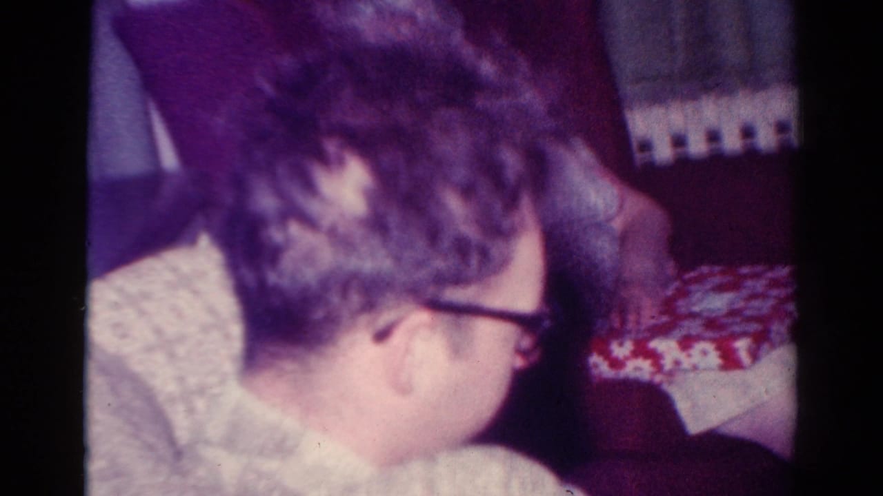 Man with glasses turns his head beside a red-and-white patterned box and radiator.