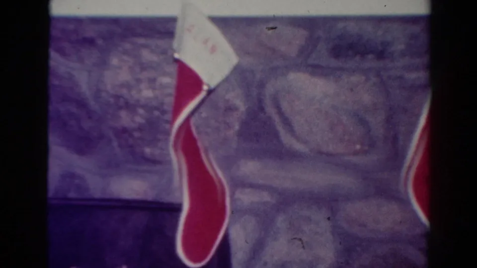 Close 8mm view of a Christmas stocking hanging below a mantel in a 1954 Toledo household interior.