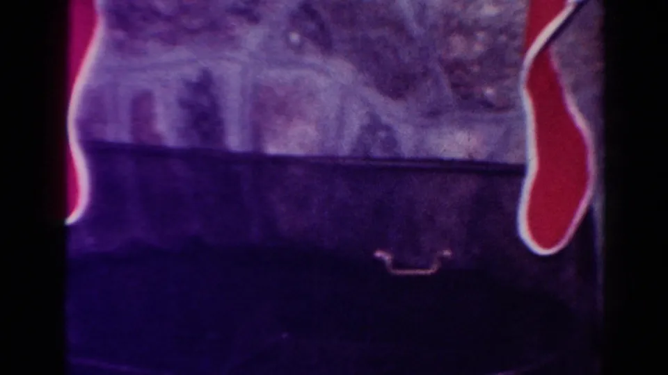 Lower 1954 home-movie frame showing red Christmas stockings at the sides of a fireplace hearth, with dark interior shadow below.