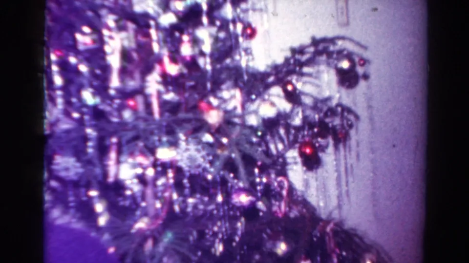 1954 Toledo holiday frame showing a Christmas tree with tinsel, lights and red ornaments beside a pale interior wall.