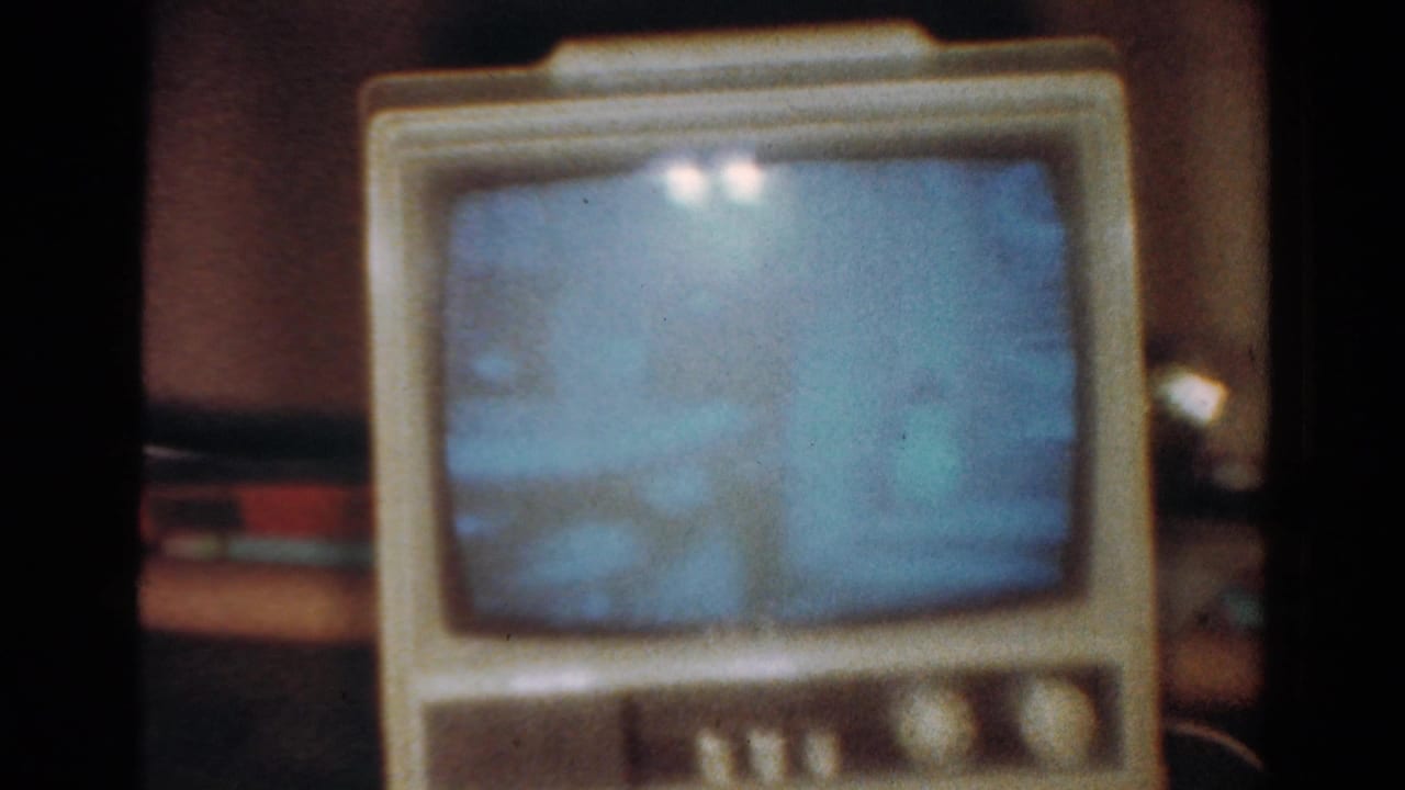 1954 Toledo home-movie frame showing a cream tabletop CRT television with a blue screen and visible 8mm film grain.