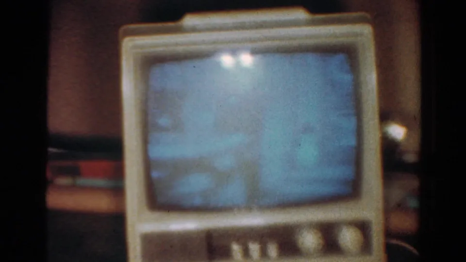 1954 Toledo home-movie frame showing a cream tabletop CRT television with a blue screen and visible 8mm film grain.