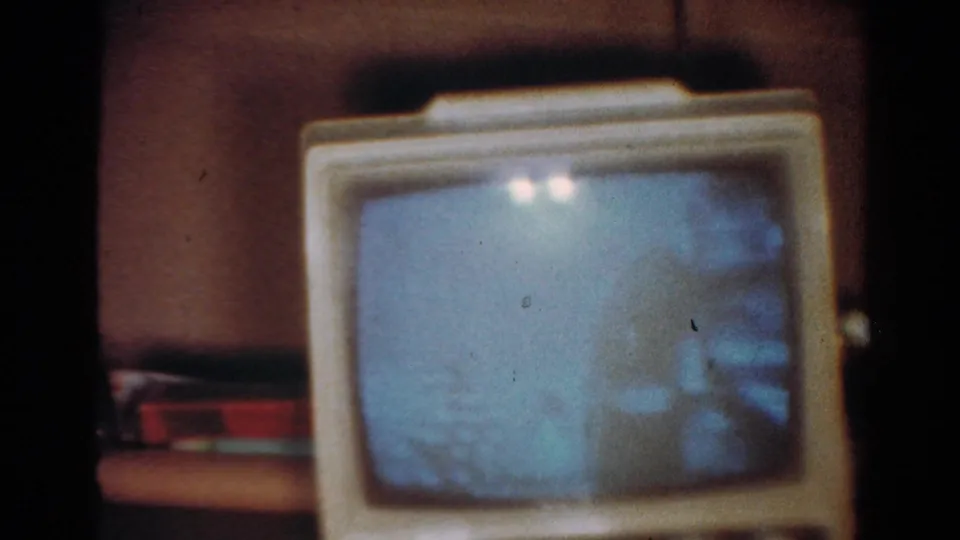 1954 Toledo home-movie still showing a vintage television set on a table, with a pale blue screen and heavy film grain.