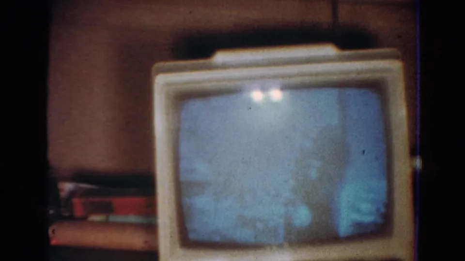 1954 Toledo frame of a cream CRT television with a blue flickering screen, filmed in soft focus on 8mm stock.