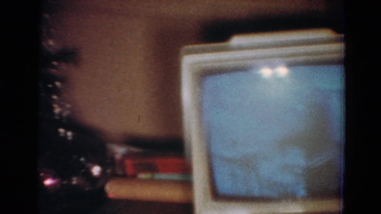 1954 Toledo home-movie frame showing a small CRT television near a Christmas tree with colored lights and tinsel.
