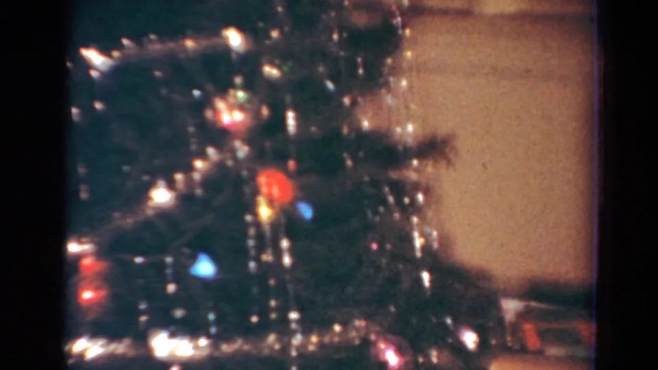 Close 1954 Toledo home-movie view of Christmas tree branches with tinsel, small ornaments, and colored lights.