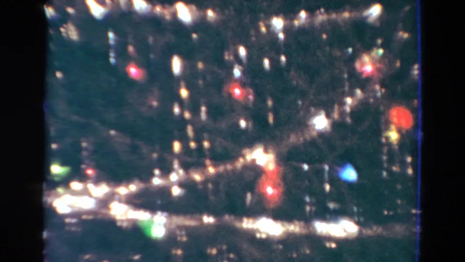1954 Toledo home-movie frame showing a tinsel-covered Christmas tree with glowing colored lights and reflective ornaments.