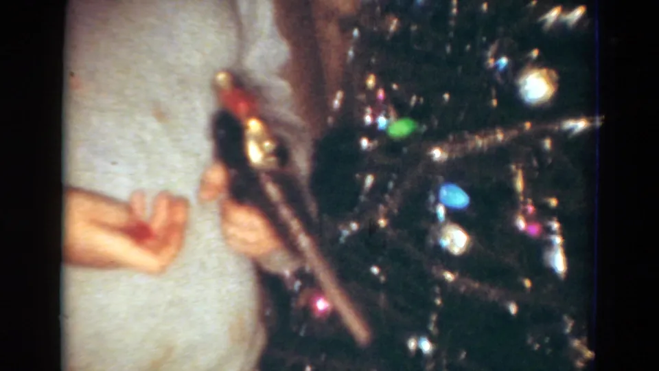 1954 Toledo frame showing a person's hands beside the Christmas tree, appearing to add or adjust an ornament among tinsel and lights.