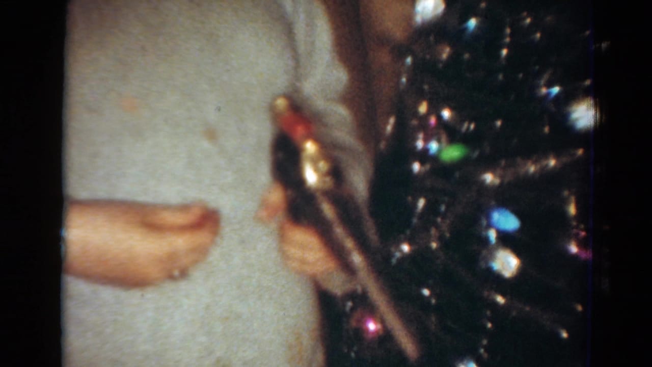 1954 Toledo home-movie frame showing cropped hands in a light sweater handling a toy gun near a shiny Christmas tree.