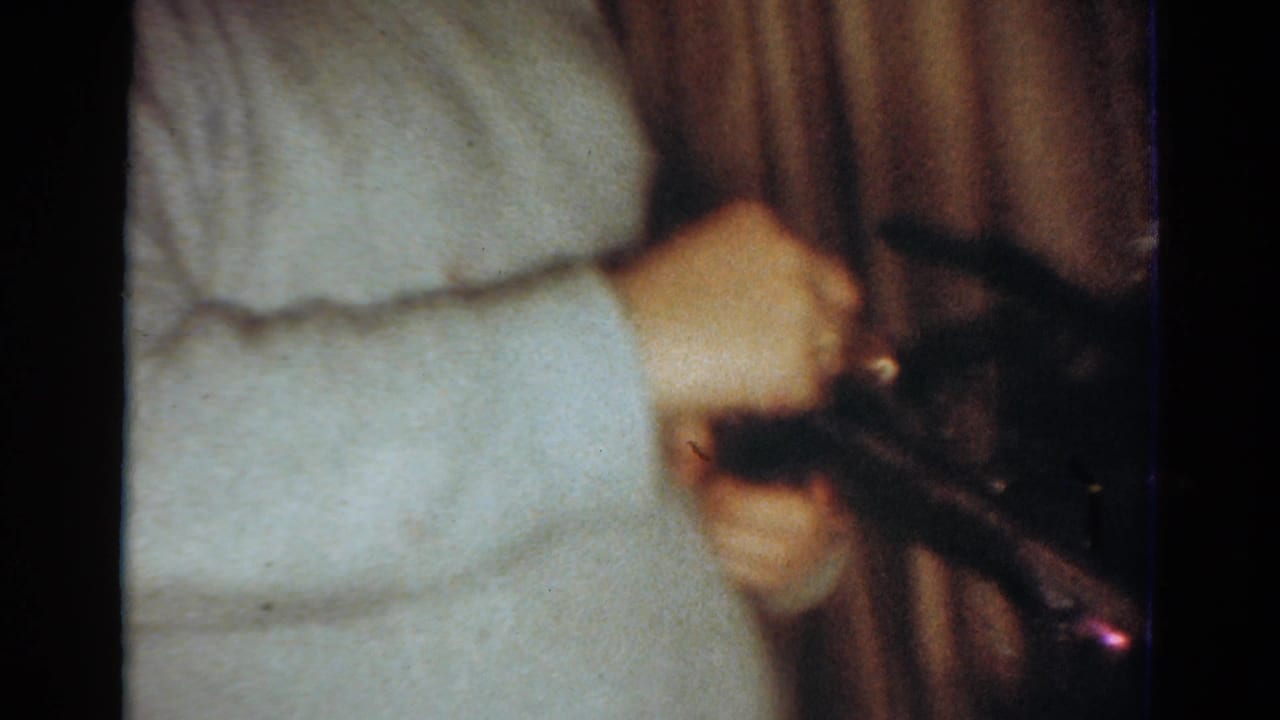 Cropped 1954 Toledo home-movie view of a person in a light sweater handling a toy gun inside a holiday room.
