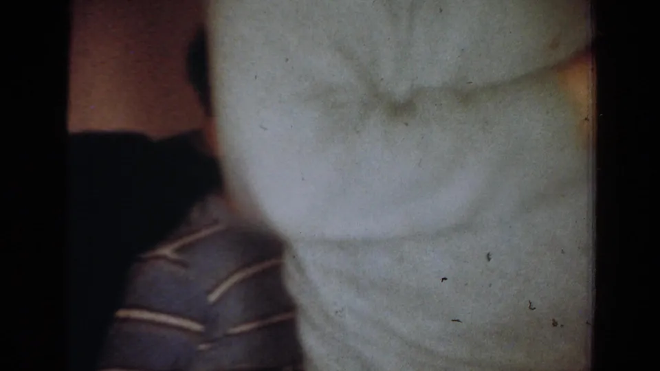 Cropped 1954 Toledo home-movie frame with a light sweater in the foreground and part of a seated person at left.