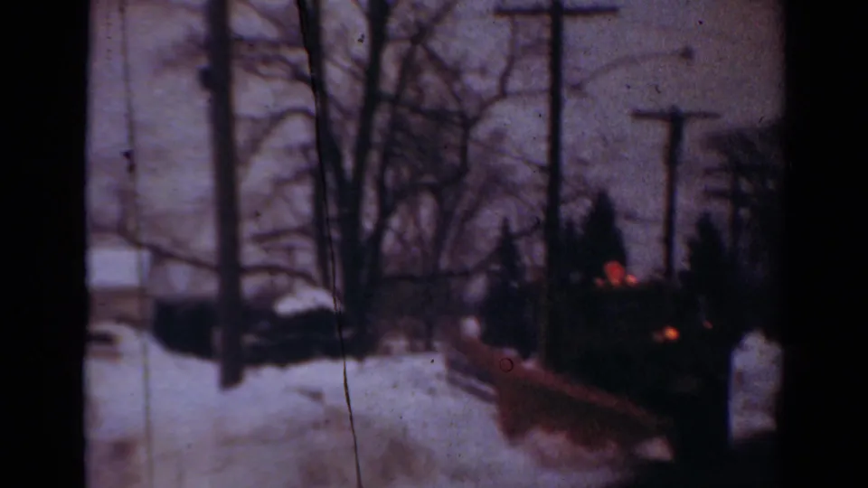 1954 Toledo winter exterior showing a snowy street, leafless trees, utility poles, and a dark vehicle in soft 8mm color.