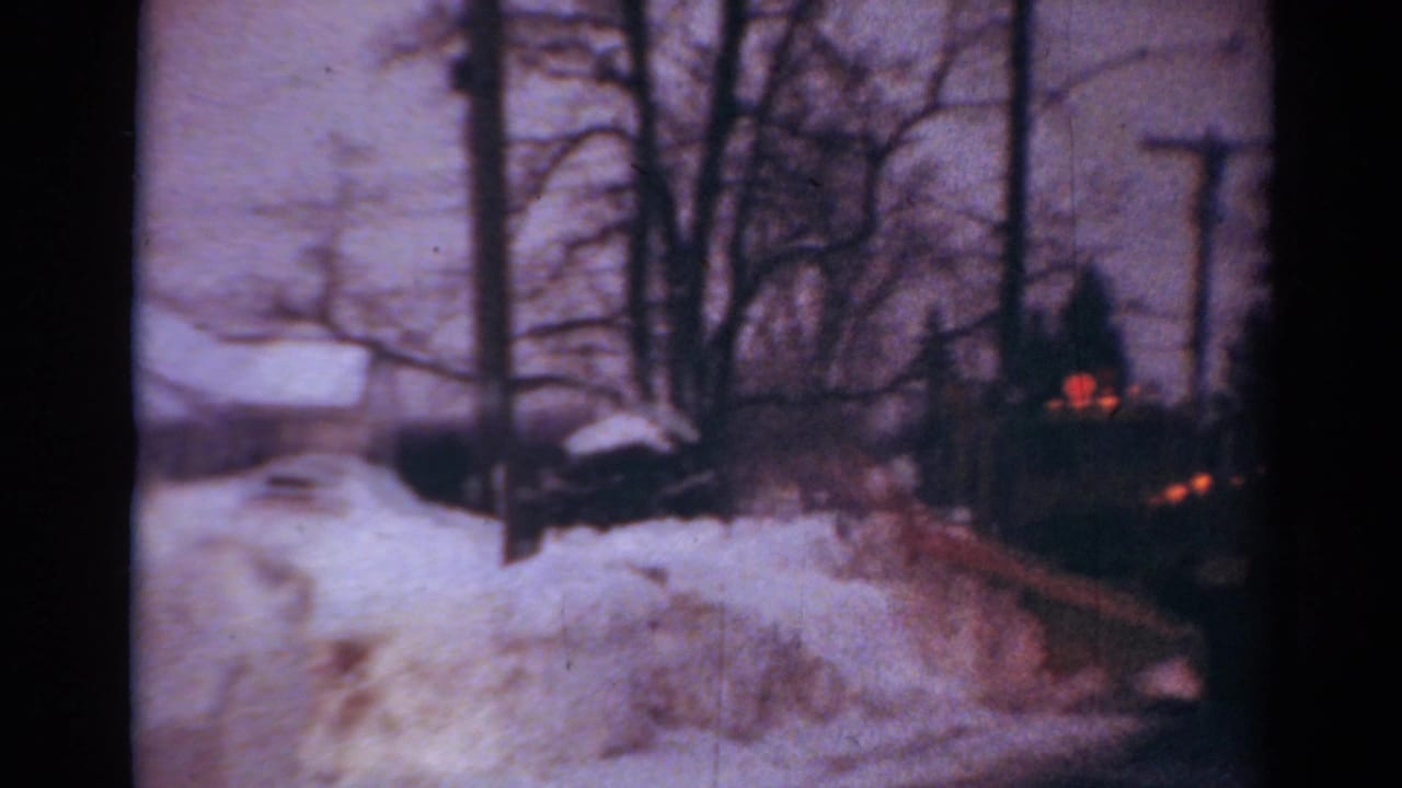 1954 Toledo home-movie frame showing a snowplow truck partly obscured by deep snow on a residential street.