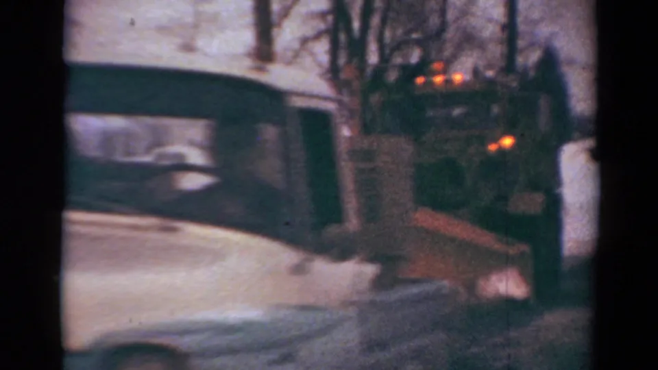 1954 Toledo street frame with a white car crossing close to the lens while a snowplow works behind it in deep snow.
