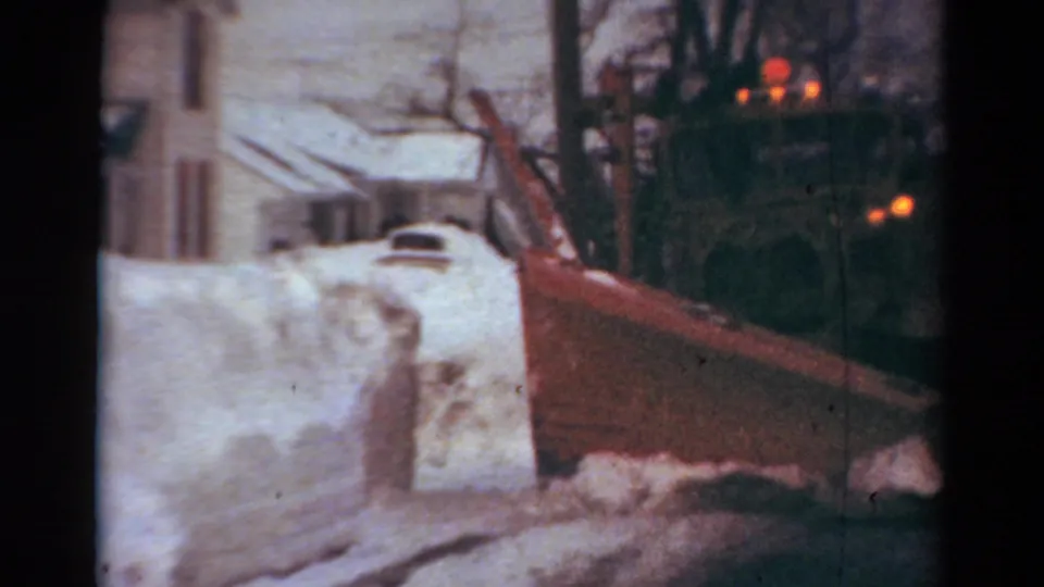 1954 Toledo home-movie view of a snowplow blade moving past high snowbanks on a residential winter street.